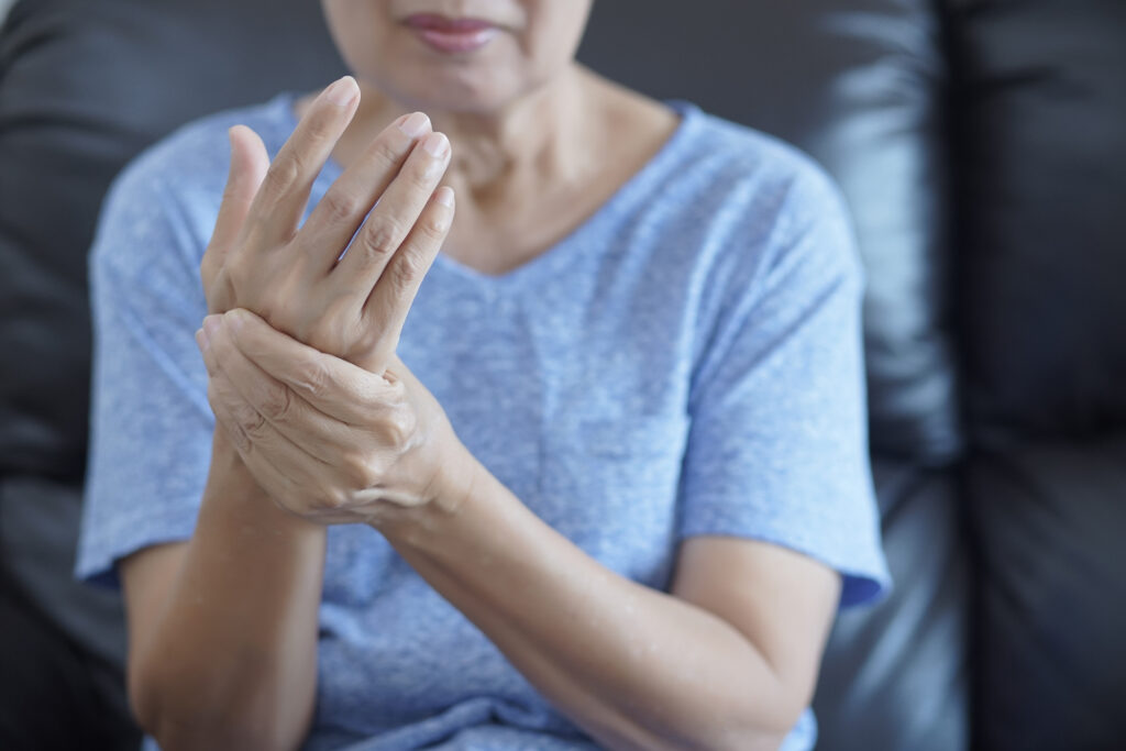 Image of a lady wearing a blue tshirt who is holding her right wrist with her left hand to depict arthritus