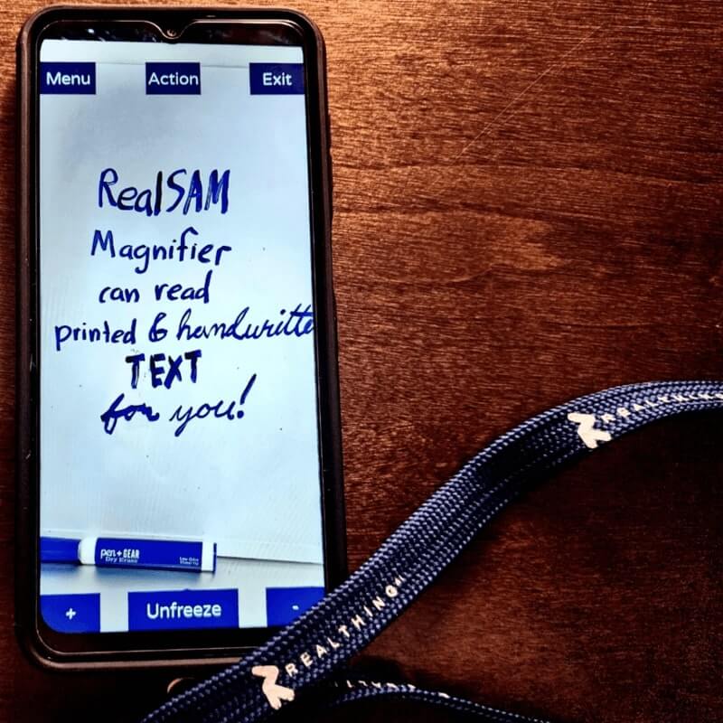 A Real Sam Pocket smart phone in magnifer mode. The text on the screen reads Real Sam magnifier can read printed and handwritten text for you!