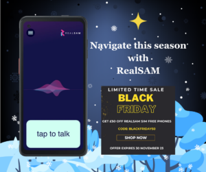 On the left is the RealSAM Pocket with the ‘tap to talk’ button activated. On the right is a 4-point gold star. Below that it says, ‘Navigate this season with RealSAM.’ Below that is a black square with gold flecks and gold writing on all caps saying, ‘Limited time sale. Black Friday. Get £50 off RealSAM SIM free phones. Code: BLACKFRIDAY50. Shop Now. Offer expires 30 November 23.’ The background is a dark blue night sky dotted with snowflakes and stars. At the bottom there’s a snowy landscape with bare trees.