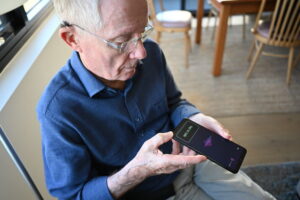 Man in his 70s wearing glasses holds a Real Sam Pocket Plus device