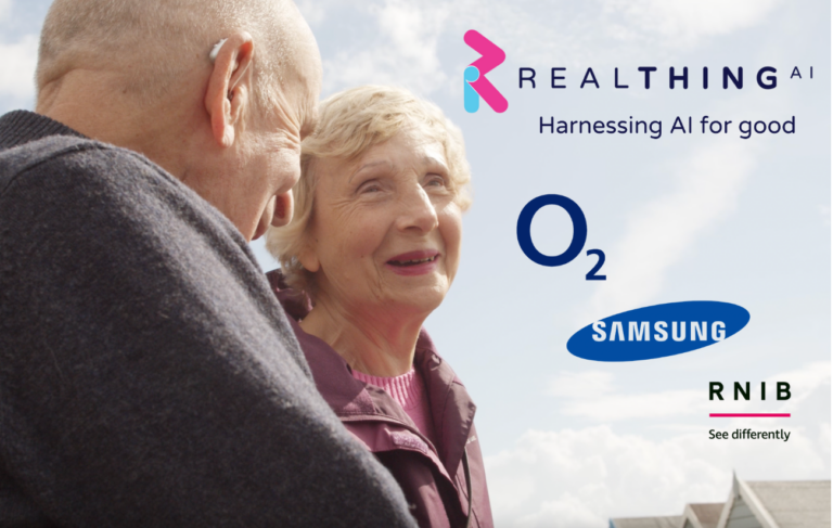 An elderly couple are smiling outdoors under a blue sky. The RealThing AI logo is displayed, below which the phrase "Harnessing AI for good" is written. The logos for Virgin Media O2, Samsung, and the RNIB in the background emphasise the collaboration towards enhancing accessible technology.