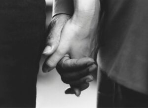 A black and white photo of two hands—those of an elderly parent and their child—gently clasped together, conveying a sense of connection and intimacy. The image represents supporting someone with sight loss.