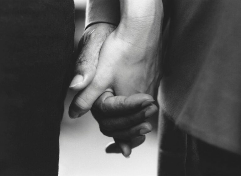 A black and white photo of two hands—those of an elderly parent and their child—gently clasped together, conveying a sense of connection and intimacy. The image represents supporting someone with sight loss.