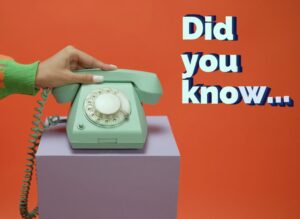 A hand in a green sleeve holds a mint green landline rotary phone, which sits on a purple pedestal against an orange background. The text reads, "Did you know...", in retro script.