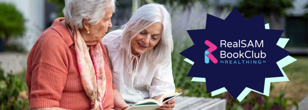 Two ladies sitting on a park bench with the logo for Real Sam bookclub on their right